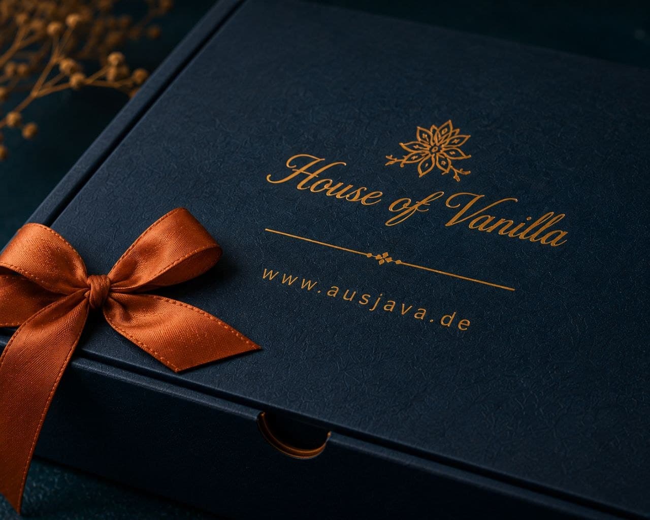 The closed navy gift box with brass foil logo and terracotta ribbon